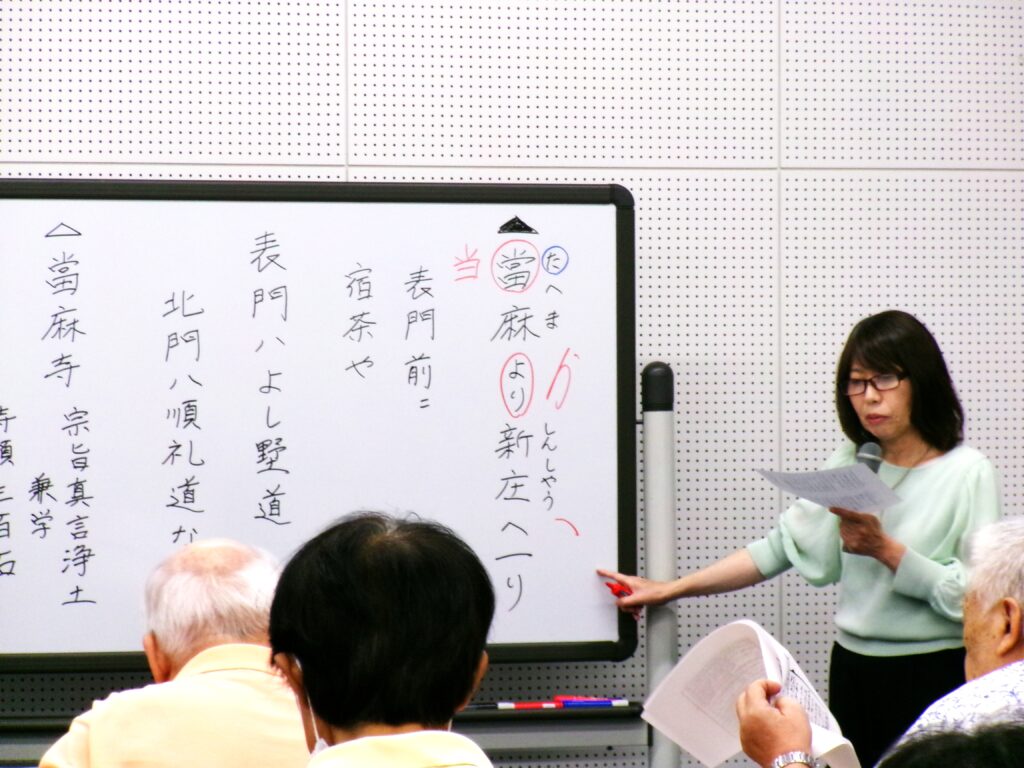講座の画像。ホワイトボードの文字、「當麻より新庄へ・・・」を指さしながら講師が説明している様子。