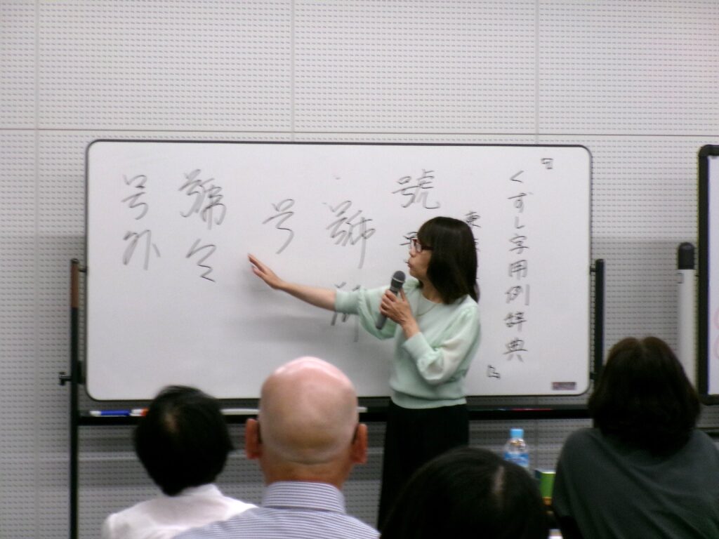講座の画像。ホワイトボードに「くずし字用例辞典」の文字。講師が説明している。