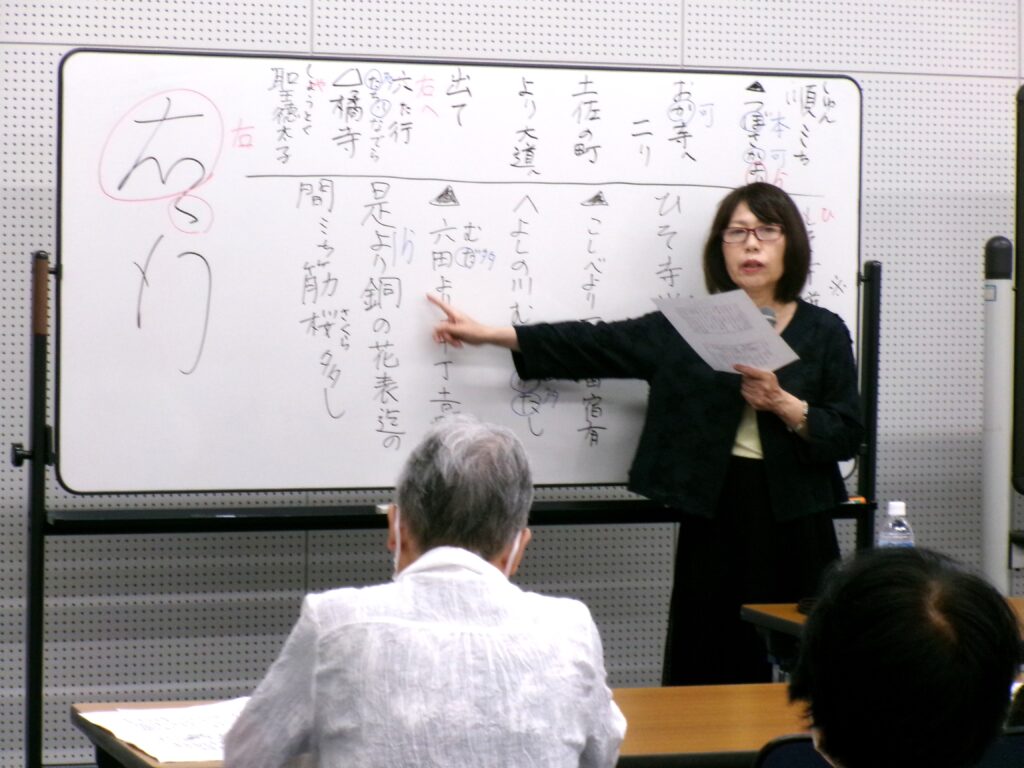 講座の画像。ホワイトボードに書かれた「是より銅の花表迄の」を指さし説明している先生。